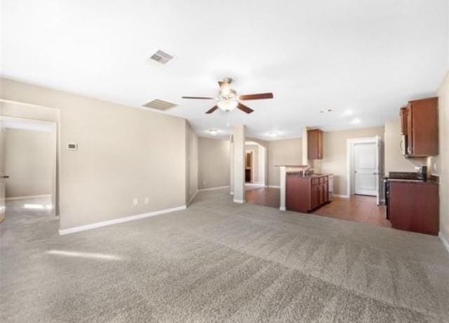 unfurnished living room with ceiling fan and dark colored carpet