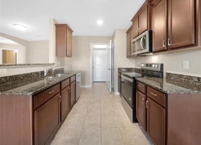 kitchen with sink, stainless steel appliances, dark stone counters, and light tile patterned flooring