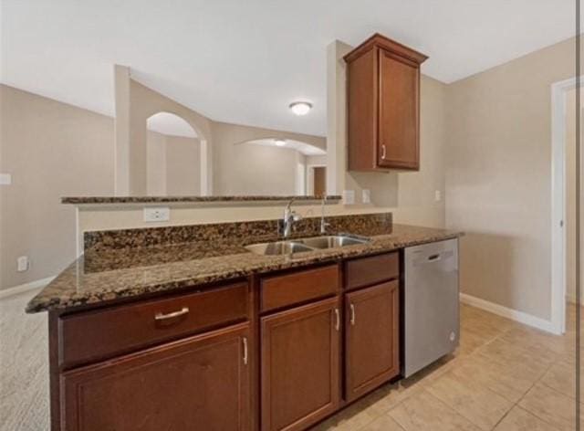 kitchen with light tile patterned flooring, sink, dishwasher, kitchen peninsula, and dark stone counters