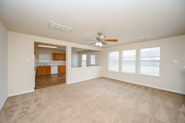 unfurnished living room featuring sink, light colored carpet, and ceiling fan