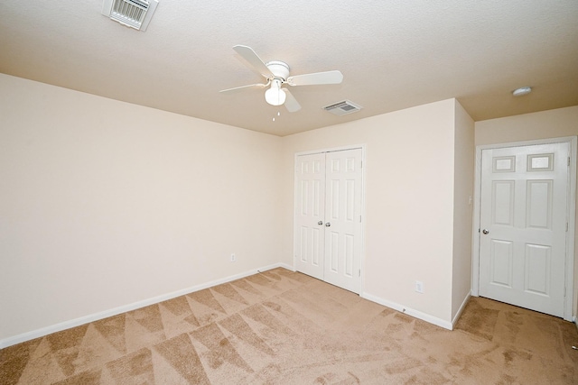 unfurnished bedroom featuring ceiling fan, a closet, light carpet, and a textured ceiling