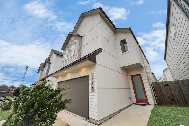 contemporary house with board and batten siding, a garage, and fence