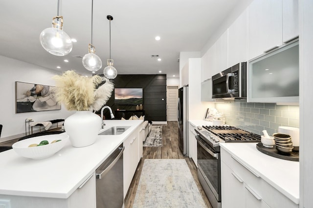 kitchen featuring white cabinetry, tasteful backsplash, hanging light fixtures, a center island with sink, and appliances with stainless steel finishes