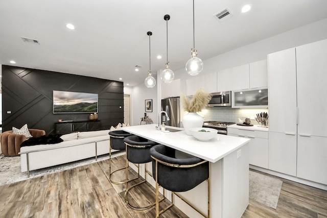 kitchen featuring a breakfast bar, white cabinetry, a center island with sink, appliances with stainless steel finishes, and decorative backsplash