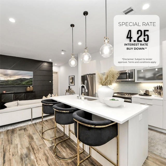 kitchen featuring visible vents, backsplash, white cabinetry, stainless steel appliances, and light wood finished floors