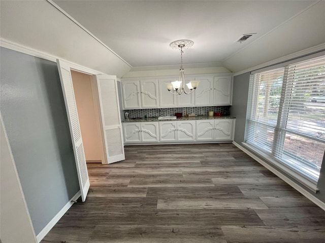 kitchen with pendant lighting, lofted ceiling, tasteful backsplash, white cabinets, and a chandelier