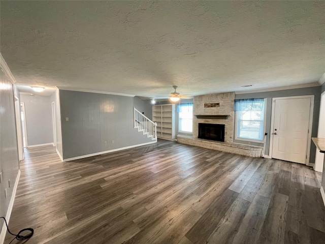 unfurnished living room with dark wood-type flooring, a textured ceiling, ornamental molding, ceiling fan, and a fireplace