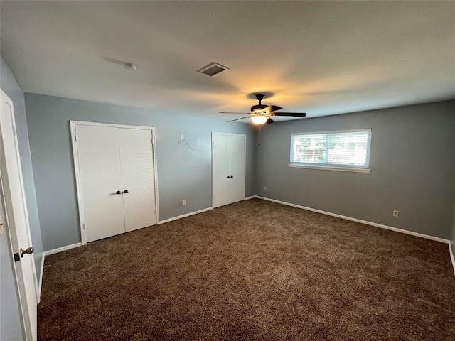 unfurnished bedroom featuring ceiling fan, multiple closets, and dark colored carpet