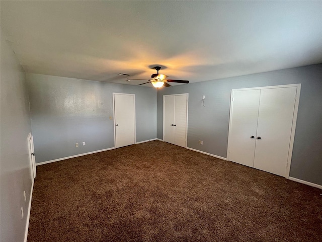 unfurnished bedroom featuring ceiling fan, two closets, and dark carpet