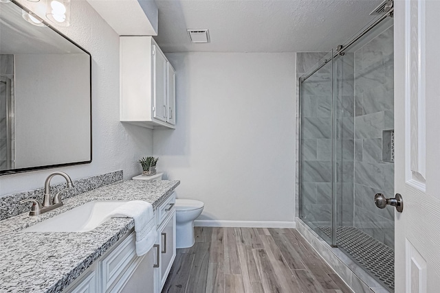 bathroom with wood-type flooring, vanity, toilet, a shower with door, and a textured ceiling