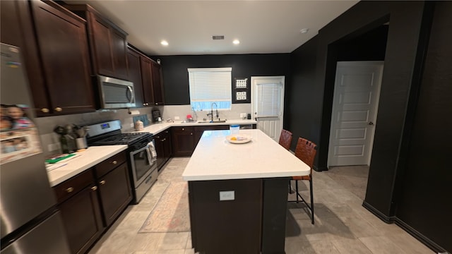 kitchen with sink, a center island, dark brown cabinets, appliances with stainless steel finishes, and a kitchen breakfast bar