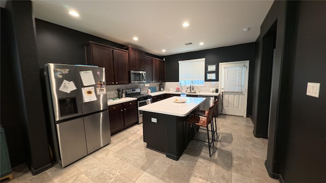 kitchen with sink, a center island, dark brown cabinets, appliances with stainless steel finishes, and a kitchen breakfast bar