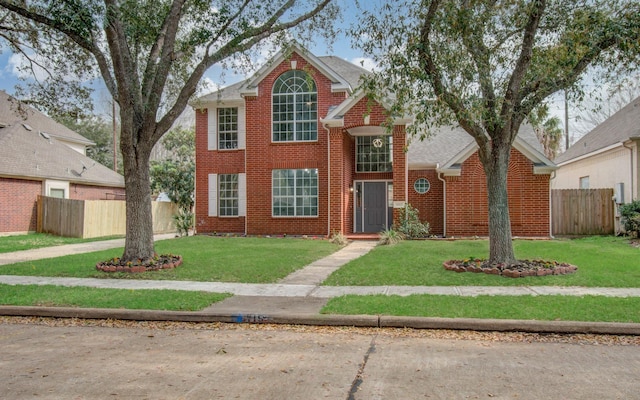 traditional-style house featuring a front yard, brick siding, and fence