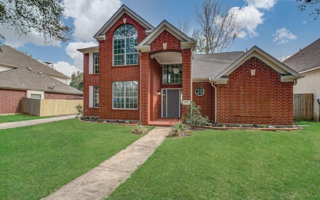 traditional-style home featuring a front yard, brick siding, and fence