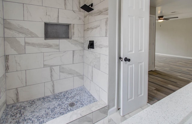 full bathroom with a ceiling fan, a tile shower, baseboards, and wood finished floors