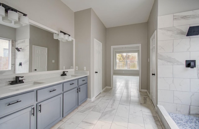 full bath with marble finish floor, tiled shower, a sink, and double vanity