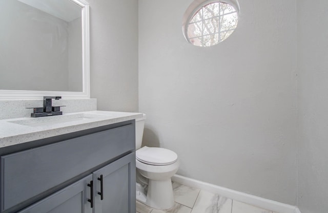 half bath with toilet, marble finish floor, baseboards, and vanity