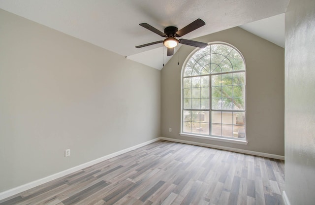 empty room featuring ceiling fan, baseboards, vaulted ceiling, and wood finished floors