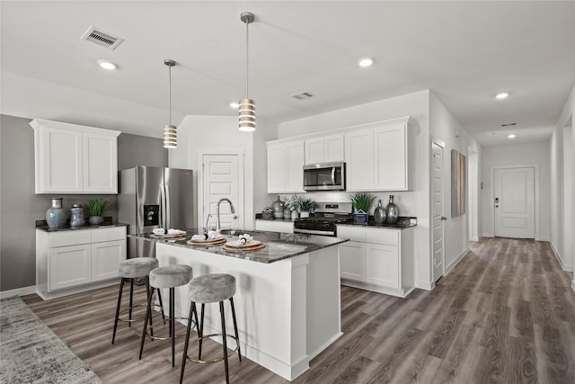 kitchen featuring stainless steel appliances, pendant lighting, a center island with sink, and white cabinets