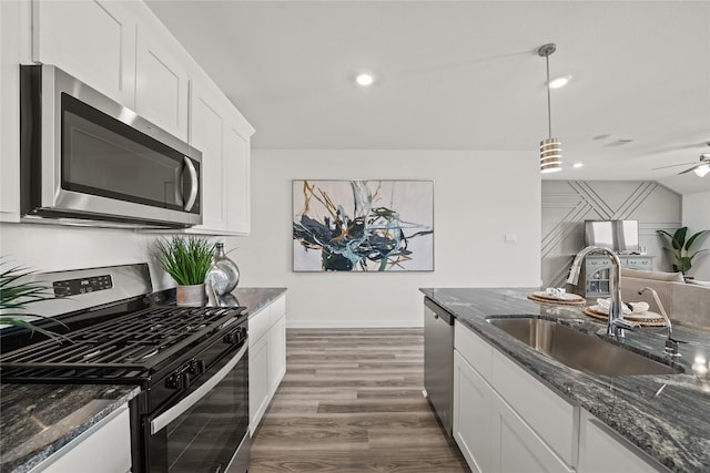 kitchen featuring sink, decorative light fixtures, dark stone countertops, stainless steel appliances, and white cabinets