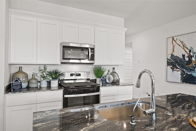 kitchen with dark stone countertops, sink, stainless steel appliances, and white cabinets