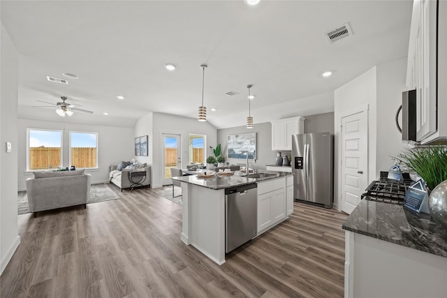 kitchen featuring wood-type flooring, decorative light fixtures, stainless steel appliances, a kitchen island with sink, and white cabinets