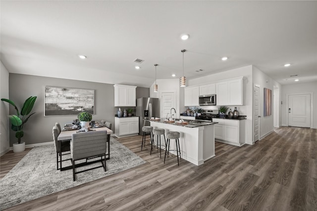 kitchen with a breakfast bar, appliances with stainless steel finishes, white cabinetry, hanging light fixtures, and an island with sink