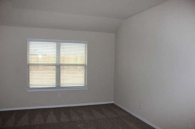 empty room featuring lofted ceiling, dark carpet, and baseboards