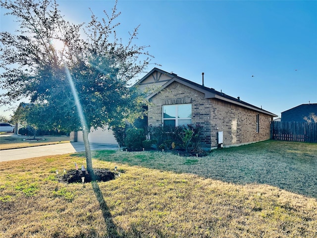 view of side of home with driveway, brick siding, fence, and a yard