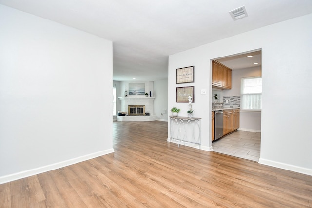 kitchen featuring stainless steel dishwasher, a fireplace, light wood-type flooring, and decorative backsplash