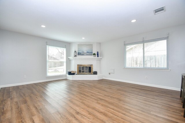 unfurnished living room featuring wood-type flooring and a brick fireplace