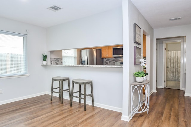 kitchen featuring a kitchen bar, light stone counters, appliances with stainless steel finishes, dark hardwood / wood-style floors, and backsplash