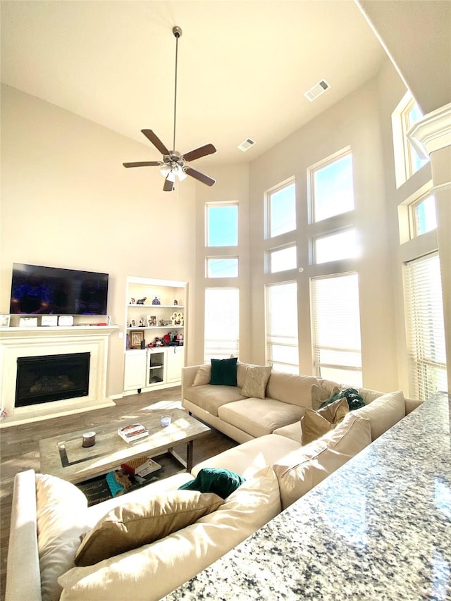 living area featuring a high ceiling, plenty of natural light, visible vents, and ceiling fan