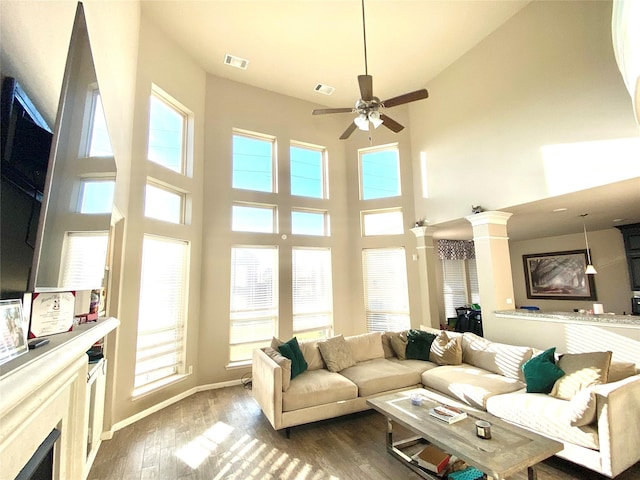 living area with dark wood-type flooring, decorative columns, a healthy amount of sunlight, and ceiling fan