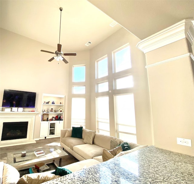 living area with visible vents, a fireplace with raised hearth, wood finished floors, a high ceiling, and ceiling fan