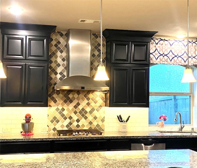 kitchen with light stone countertops, stainless steel appliances, wall chimney range hood, and a sink