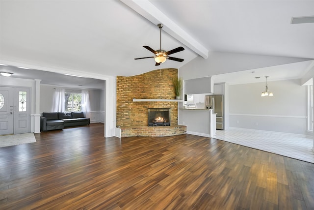 unfurnished living room with lofted ceiling with beams, a brick fireplace, ceiling fan with notable chandelier, and dark hardwood / wood-style flooring