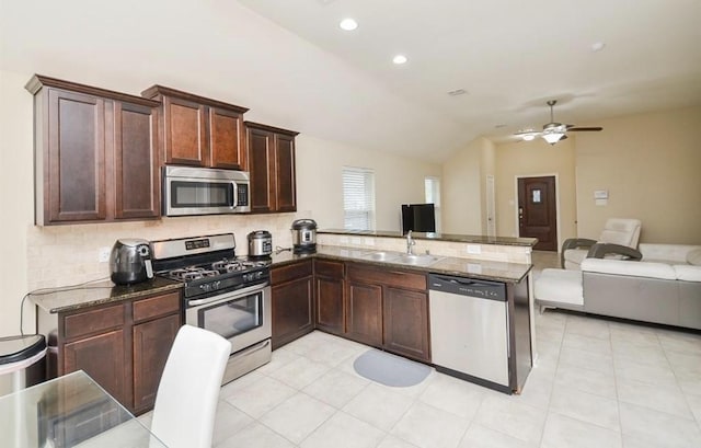 kitchen featuring sink, vaulted ceiling, dark stone counters, kitchen peninsula, and stainless steel appliances