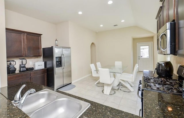 kitchen with lofted ceiling, sink, light tile patterned floors, appliances with stainless steel finishes, and dark stone countertops