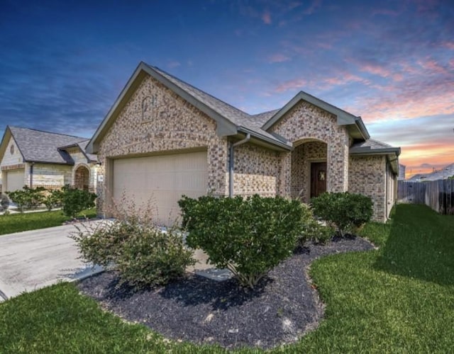 ranch-style home with fence, concrete driveway, a yard, a garage, and stone siding