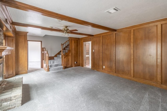 unfurnished living room with a textured ceiling, ceiling fan, wooden walls, beamed ceiling, and light colored carpet