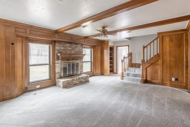 unfurnished living room with wood walls, beam ceiling, light colored carpet, a brick fireplace, and a textured ceiling