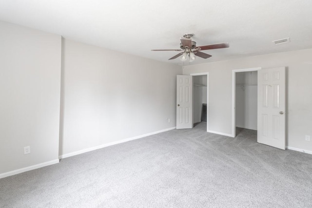 unfurnished bedroom with multiple closets, light colored carpet, and ceiling fan