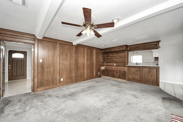 unfurnished living room with beamed ceiling, wooden walls, light carpet, and a textured ceiling