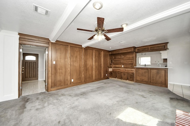 unfurnished living room with beamed ceiling, light colored carpet, a textured ceiling, and wood walls