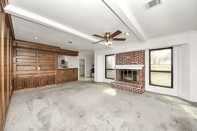 unfurnished living room featuring beamed ceiling, light colored carpet, a fireplace, and ceiling fan