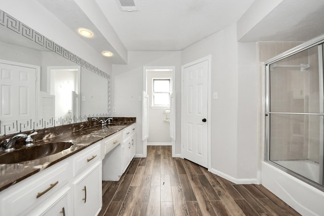 bathroom featuring wood-type flooring, vanity, and bath / shower combo with glass door