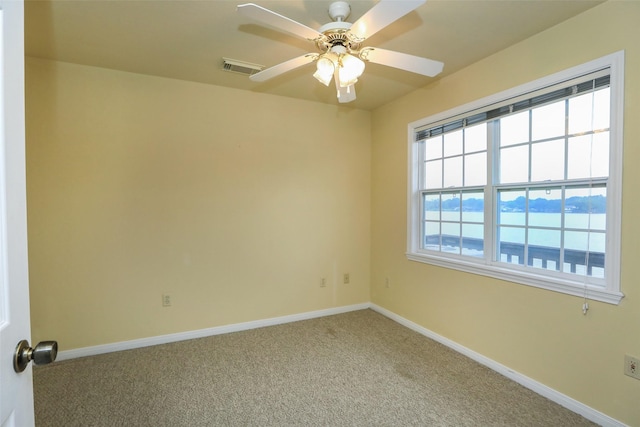 carpeted spare room with a water view and ceiling fan