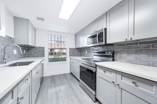 kitchen featuring sink, appliances with stainless steel finishes, light stone counters, tasteful backsplash, and light hardwood / wood-style floors