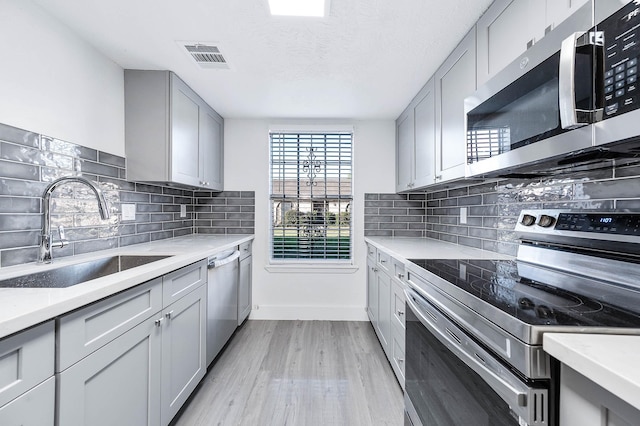 kitchen featuring gray cabinets, appliances with stainless steel finishes, tasteful backsplash, sink, and light hardwood / wood-style flooring